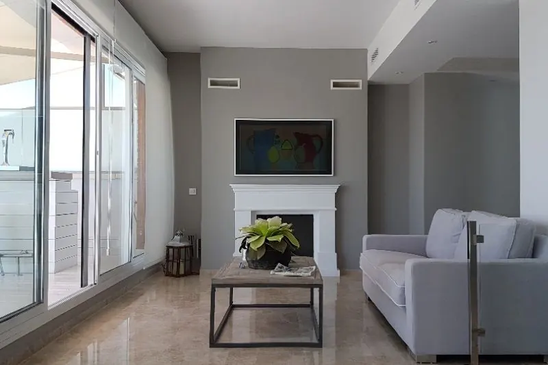 El salón, con la chimenea de mármol blanco como único elemento de fábrica. El suelo continuo y la carpintería corredera prolongan la pieza hacia la terraza.