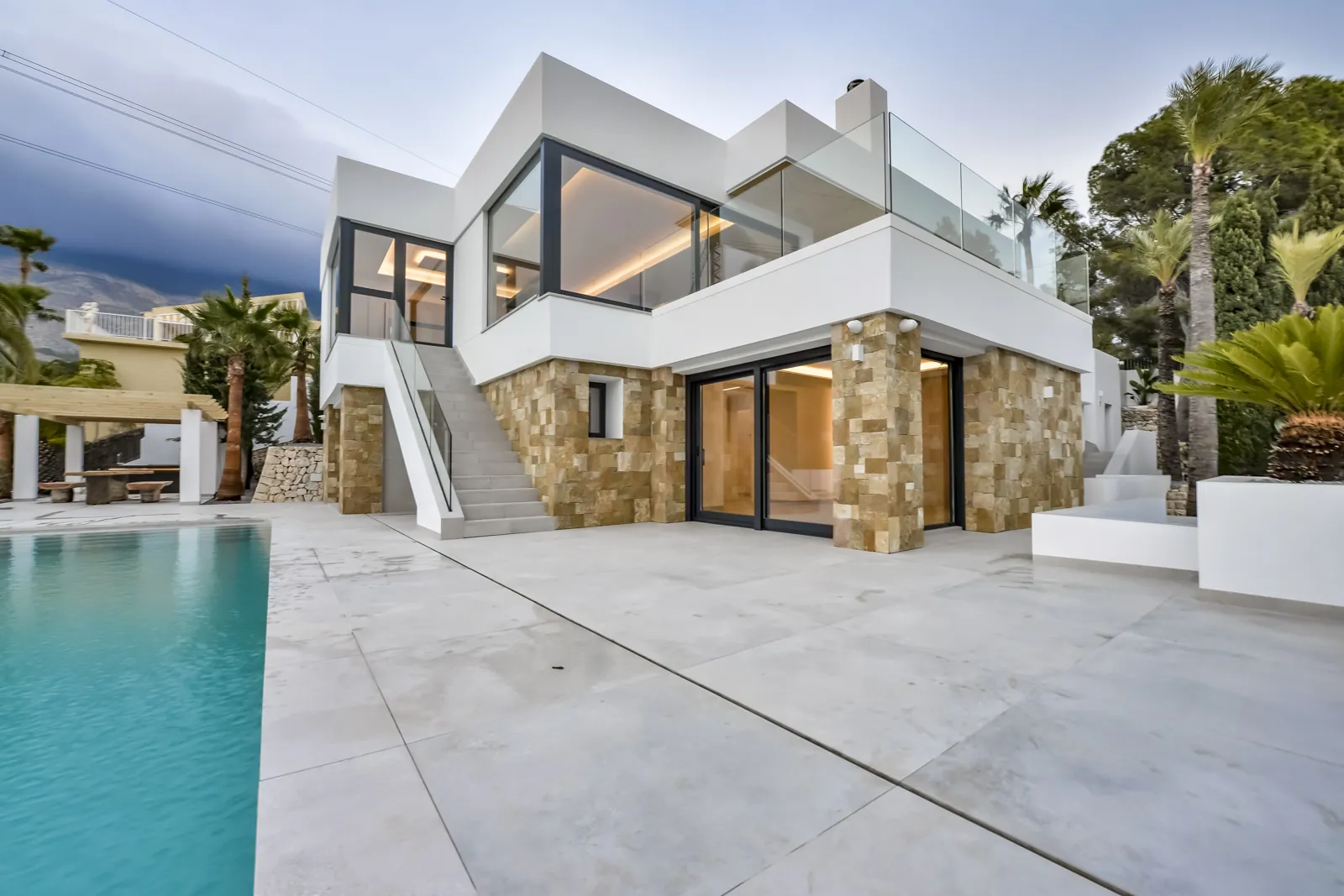 Fachada a la piscina. La planta baja se reviste de piedra dorada y la superior, blanca, vuela sobre ella; la escalera exterior comunica la terraza sin pasar por dentro.