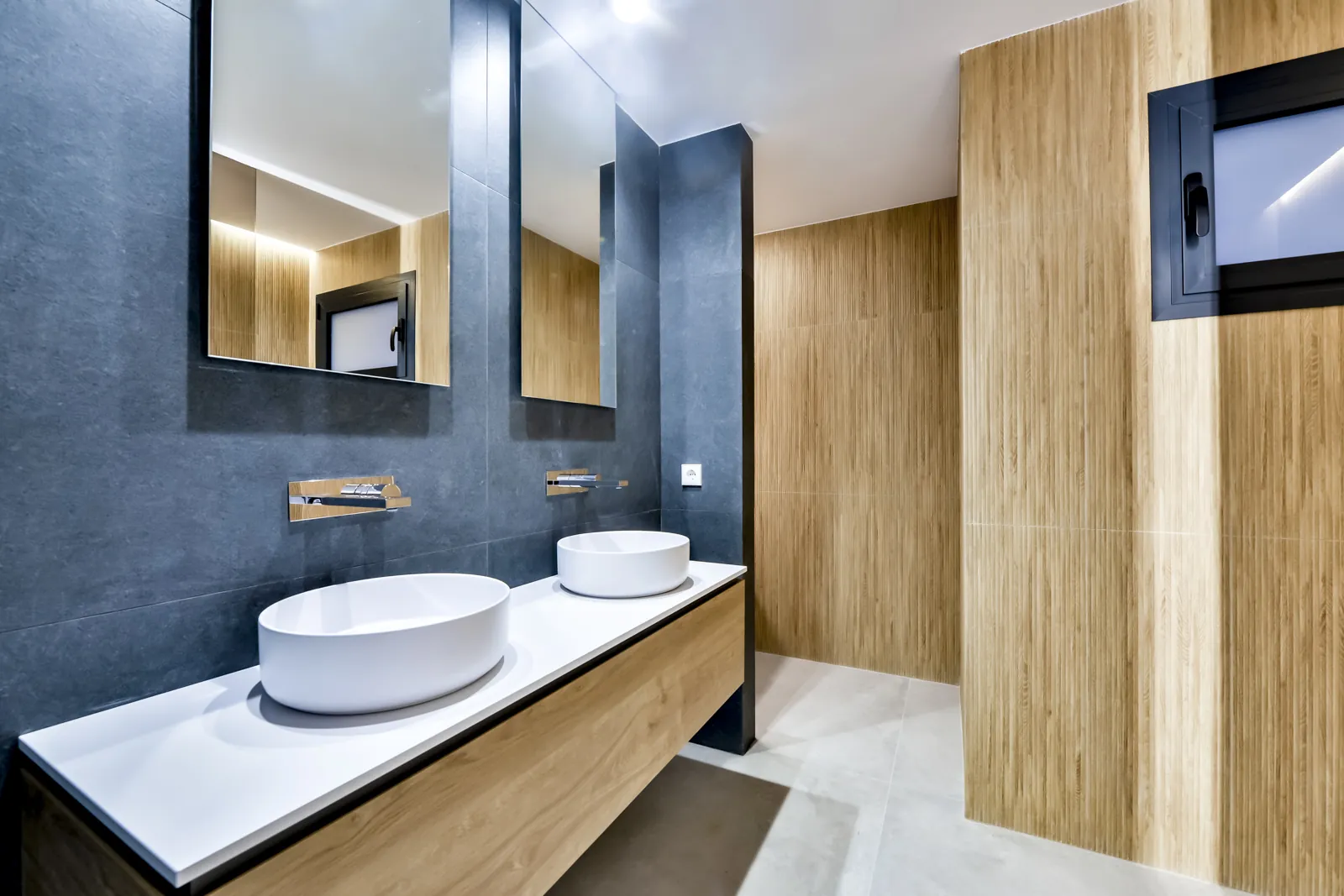 El mismo baño desde la puerta: los dos espejos repiten el revestimiento de madera de la pared opuesta y duplican la profundidad de la pieza.