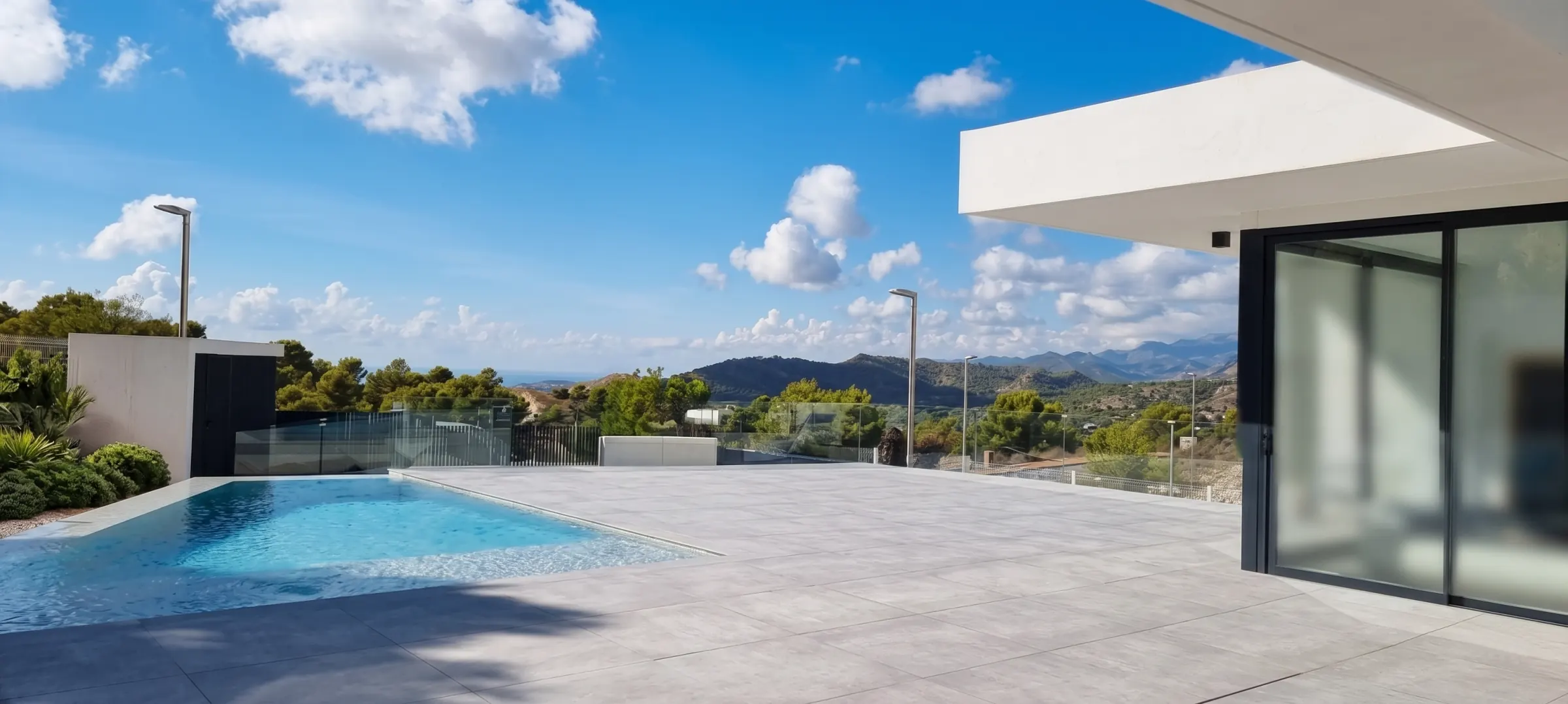La terraza se organiza en torno a la piscina, con el voladizo de la planta alta dando sombra al ventanal. El valle y la sierra quedan al otro lado del vidrio de la barandilla.
