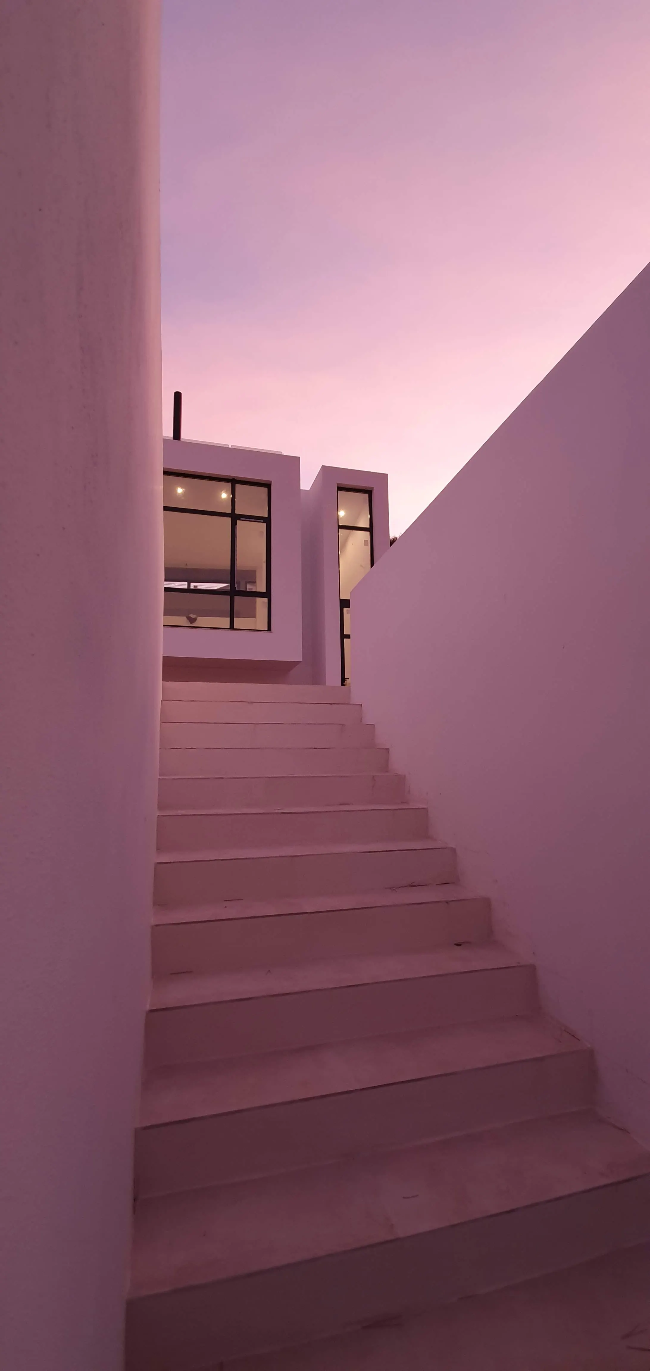 La escalera exterior sube entre dos muros encalados hasta la puerta. Al atardecer, el revoco recoge el color del cielo y el hueco iluminado marca el final del recorrido.