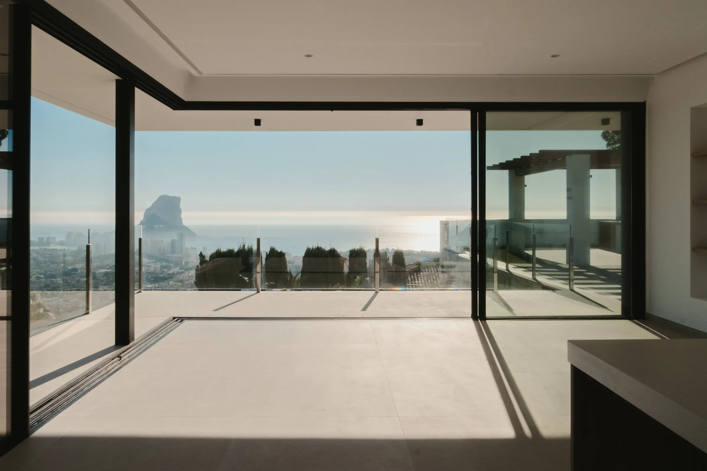 El ventanal corredero se recoge por completo y deja el salón abierto a la terraza. Enfrente, el Peñón de Ifach sobre la bahía de Calpe.